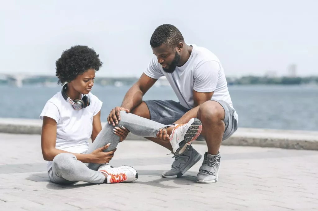 Afro Guy Helping Woman With Injured Ankle At Riverbank